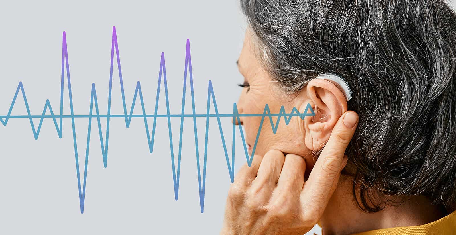 Senior woman wearing hearing aid and holding finger against ear