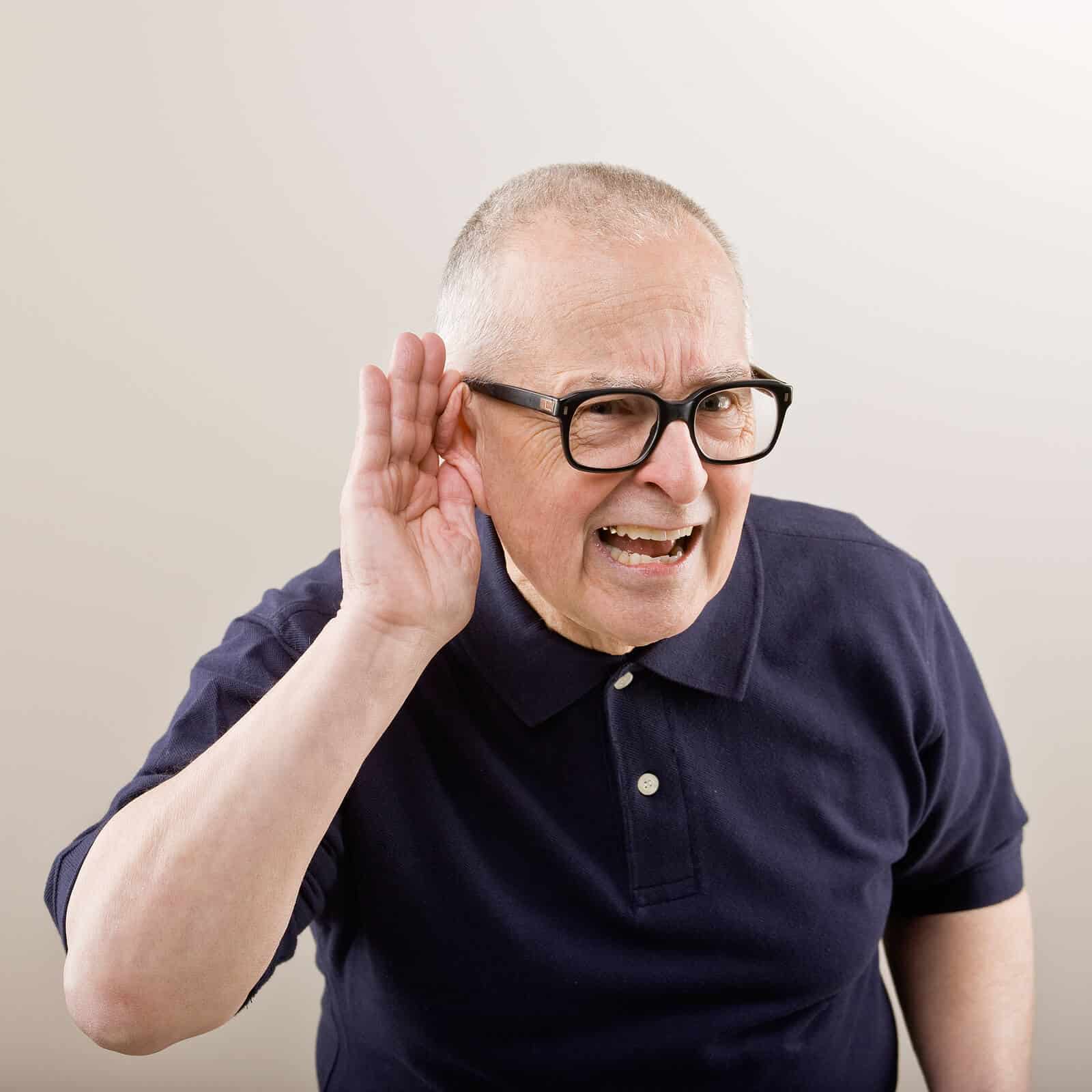 Senior man in dark blue polo shirt cupping his ear as if he cannot hear