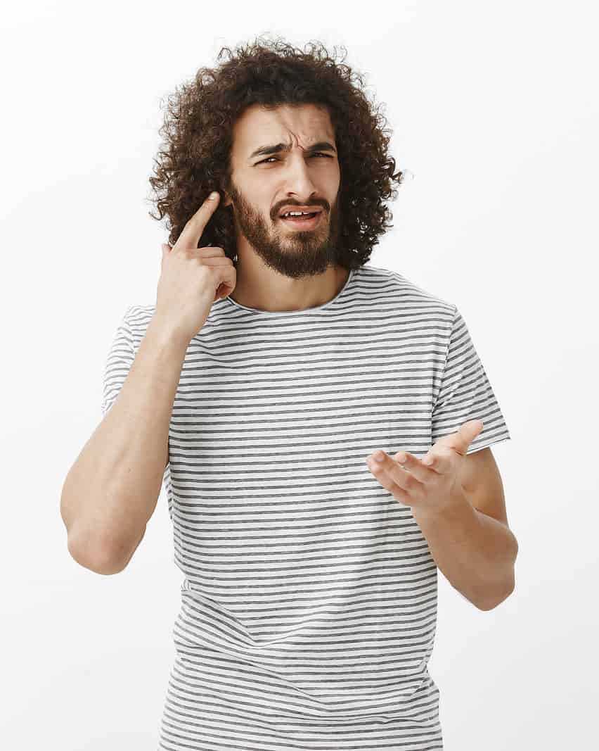 Man with striped shirt pointing at his ear like he cannot hear.