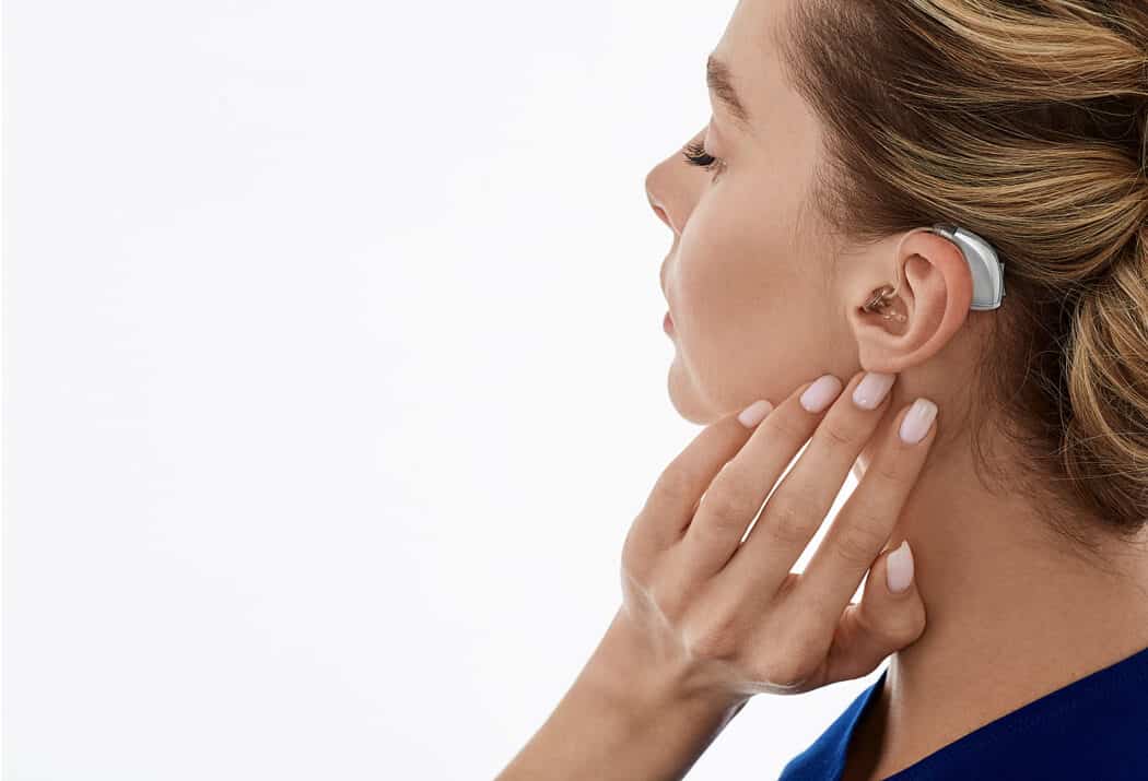 Woman holding hand under left ear with hearing aid in