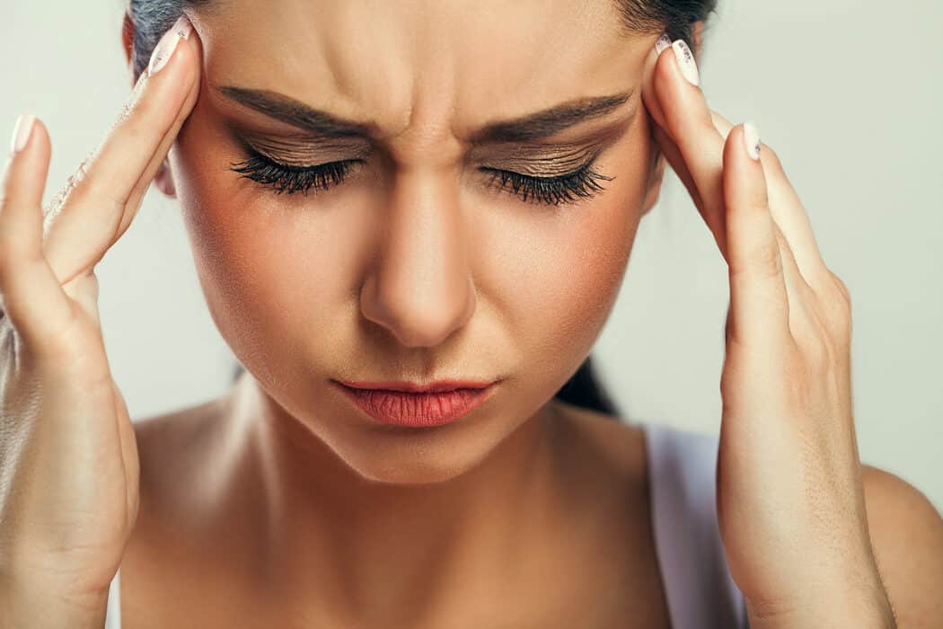 Woman holding hands against sides of head with painful look on her face due to migraine headache